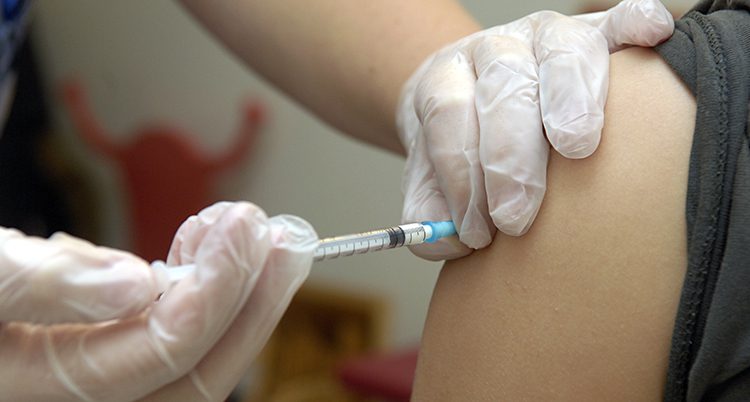 Händer med handskar sprutar in vaccin i en arm