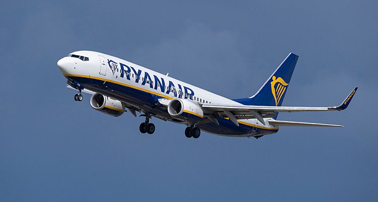 Ett flygplan som är i luften. Det är ett vitt flygplan med blå stjärt. Det står Ryanair i blått på planets sida. Himlen är blå.