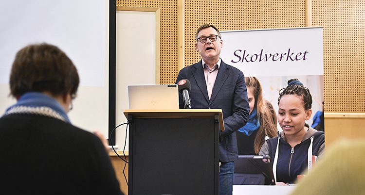 En medelålders man med glasögon pratar i mikrofon