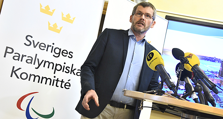 Johan Strid i kostym framför en plansch där det står Sveriges olympiska kommitté.