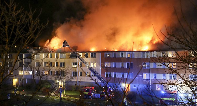 Det är mörkt och stora lågor slår upp från taket på ett stort hus.
