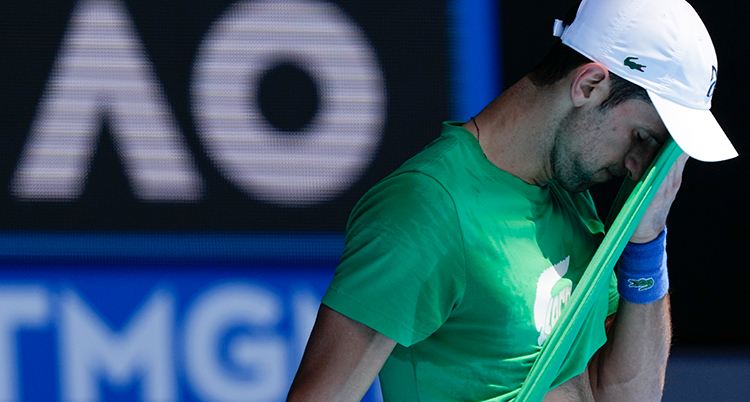 Novak Djokovic spelar tennis. Han torkar pannan med sin tröja.