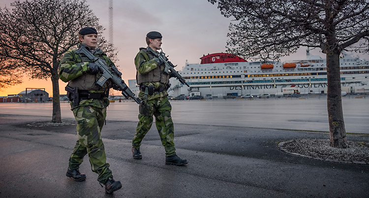 Två soldater går med vapen i Visbys hamn.