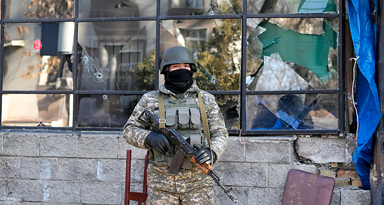 En soldat står med vapen utanför ett skadat hus.