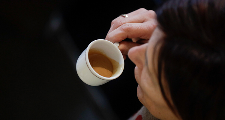 En hand håller i en liten kopp med espresso och för den mot munnen