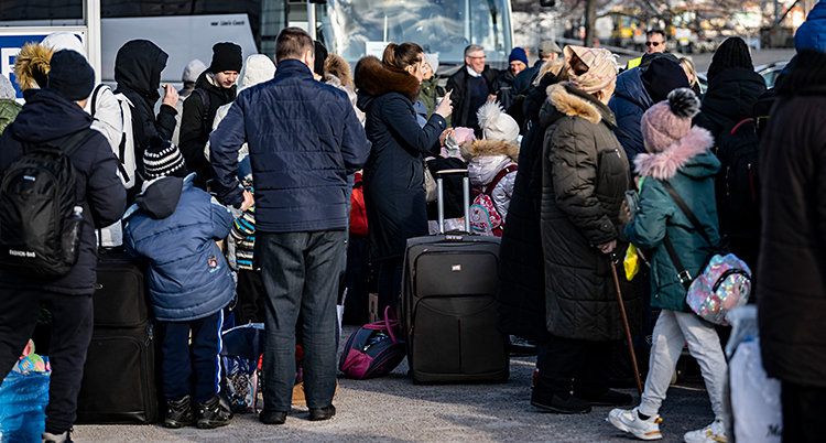 Många människor står samlade vid en buss. De har väskor med sig.