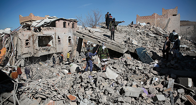 Flera människor går omkring i ruinerna av ett bombat hus.