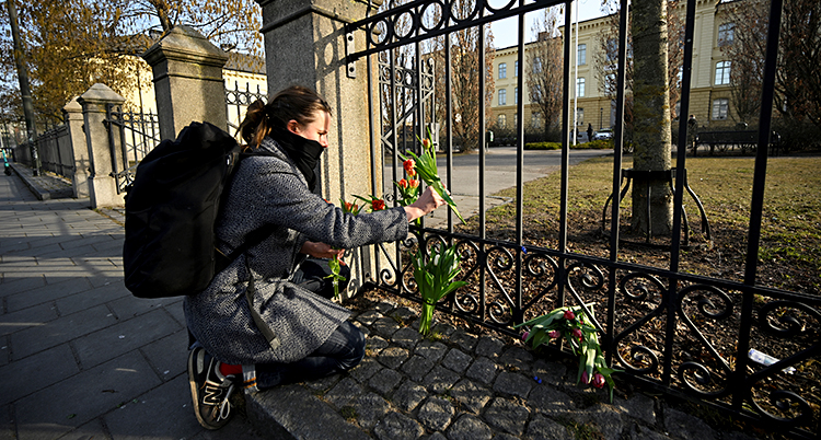 En kvinna sitter på huk och sätter fast blommor på ett staket utanför en skola.