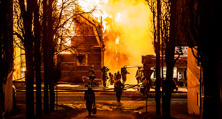 Ett hus brinner kraftigt. Några brandmän står framför.