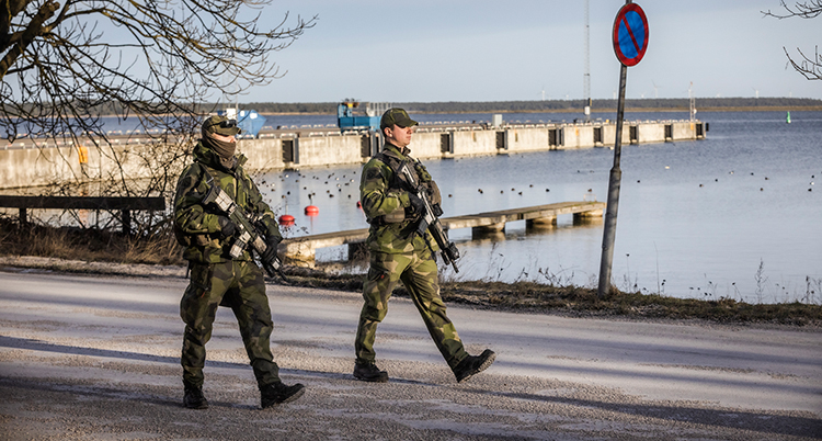 Två soldater i gröna kläder och vapen går på en gata vid havet.