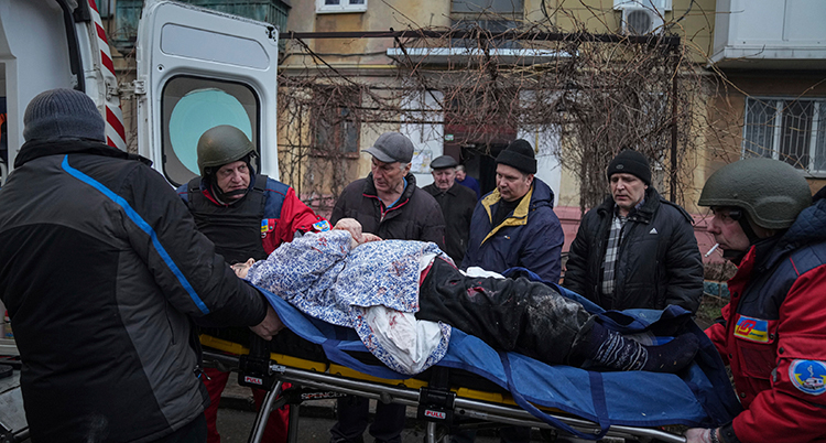 En bår med en skadad lyfts in i en ambulans. Många människor står runt.