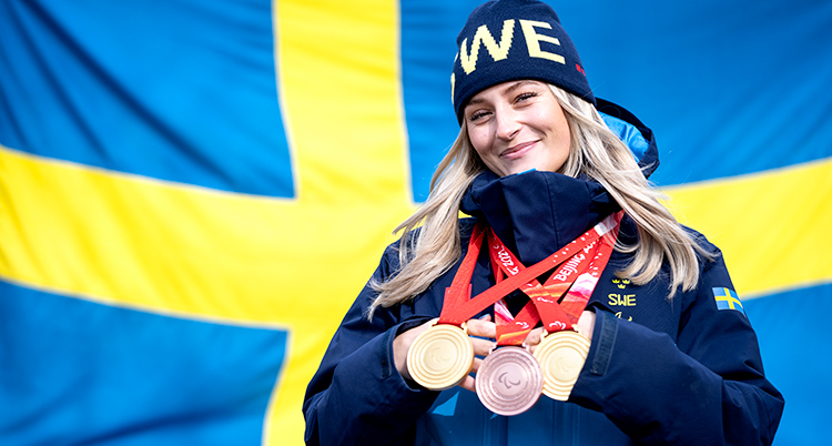 Hon står framför en svensk flagga, hon har tre medaljer runt halsen