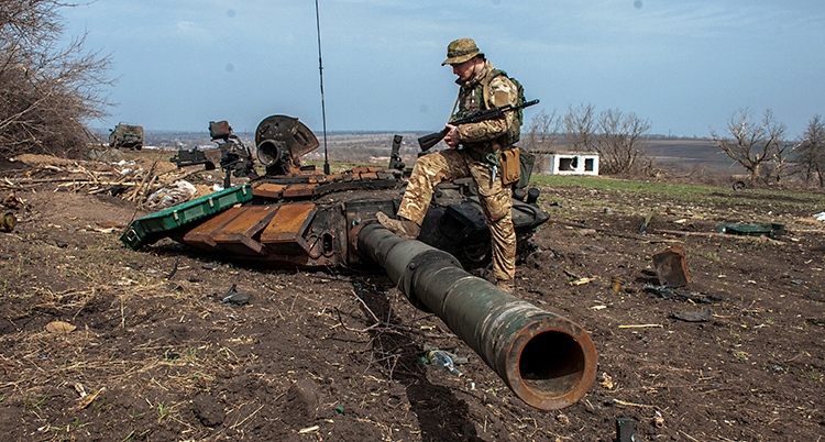 En soldat står med foten på en stridsvagn som har blivit förstörd.