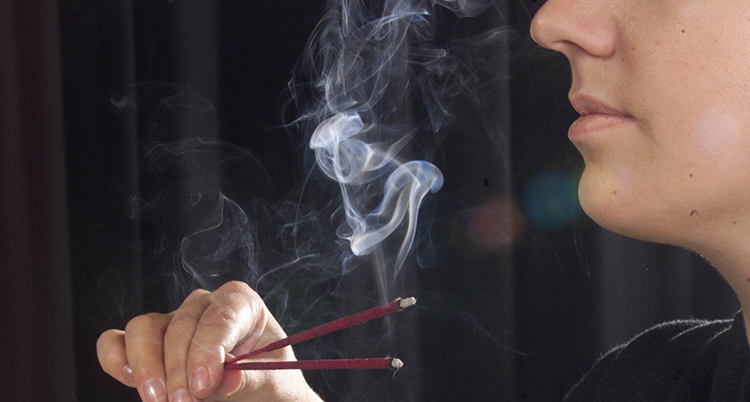 En person håller i pinnar med rökelse. Rök stiger mot näsan.