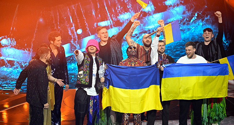 Bandet firar på scenen inför publiken. De håller upp ukrainska flaggor.