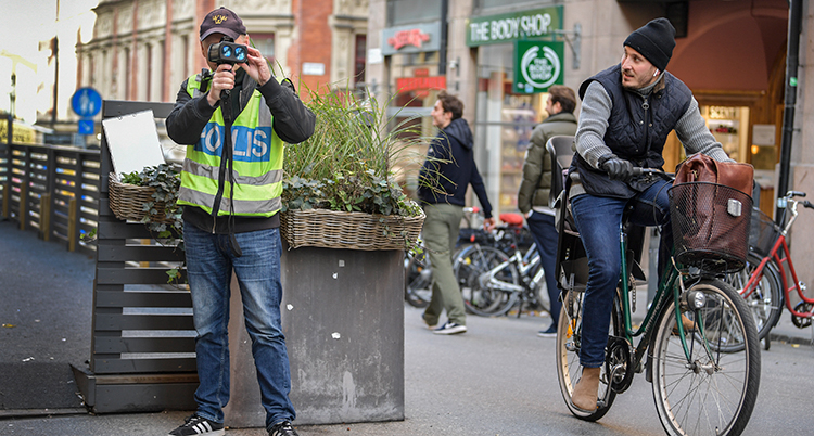 En polis tittar i en apparat. En man cyklar förbi honom.