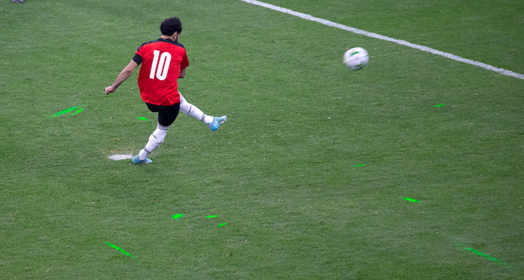 Egyptens fotbollsspelare skjuter en straff. På marken runt honom syns gröna strålar av laser.