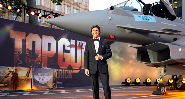 Skådespelaren står framför ett flygplan och en affisch där står Top Gun.
