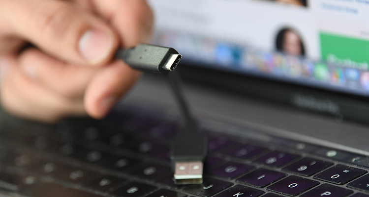 En person håller i en sladden USB-c. I bakgrunden syns en dator.