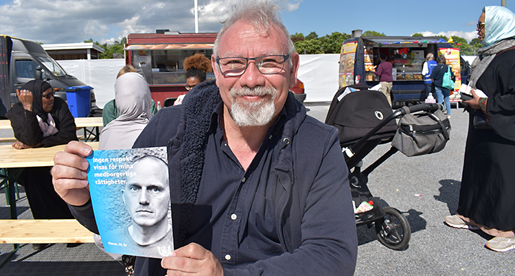 Han ler och tittar in i kameran. I sina händer håller han ett flygblad.