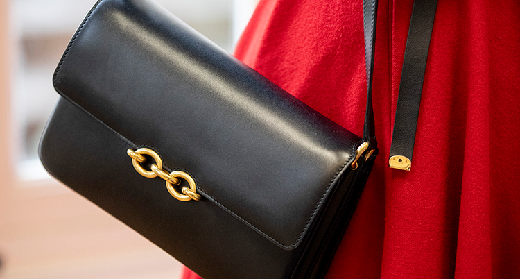 En svart handväska hänger mot en röd kappa. Det är ett guldlås på väskan.