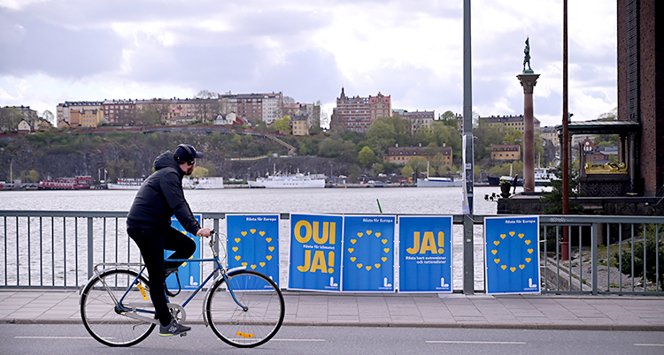 En man cyklar på en bro. Han cyklar förbi valaffischer.
