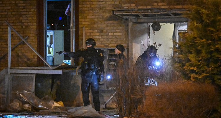 Poliser står framför en trasig port. Det är mörkt ute.