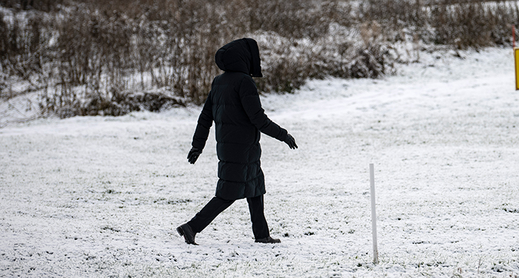 En person med mycket kläder går över en gräsmatta med snö.