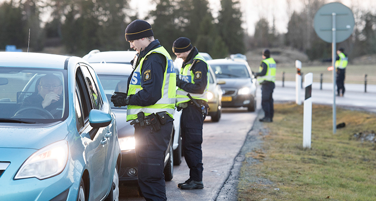 Bilar står i en rad på en väg. Poliser med gula västar står vid bilarna.