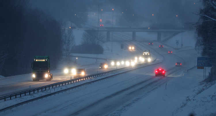 Stor väg med trafik i snöoväder. Mörk himmel.