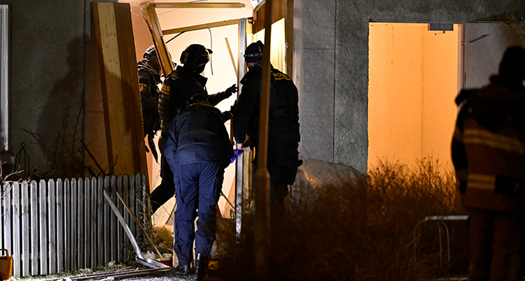Flera poliser vid en dörr som har sprängts sönder.