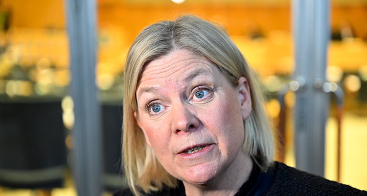 Hon har kort blont hår. Hon ser allvarlig ut.