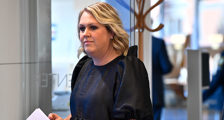 Hon har svarta kläder, ljust hår och går mot vänster.