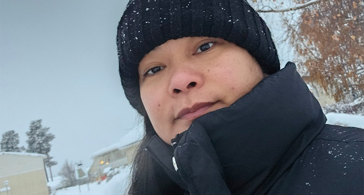 Hon har en svart mössa på sig. Det snöar på bilden.
