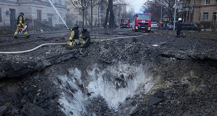En stor grop i marken mitt i en stad. Brandmän är ute och jobbar.