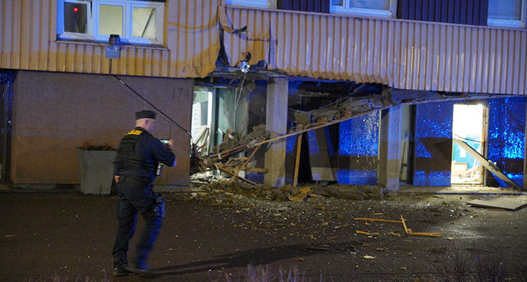 En polis syns framför fasaden till huset. Dörren är trasig. Fönster är trasiga.