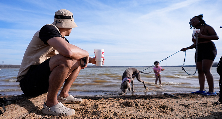 En hund och ett barn badar. Han sitter i shorts på stranden.