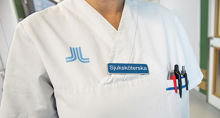 En sjuksköterska i vit dräkt. Man ser inte personens ansikte på bilden.