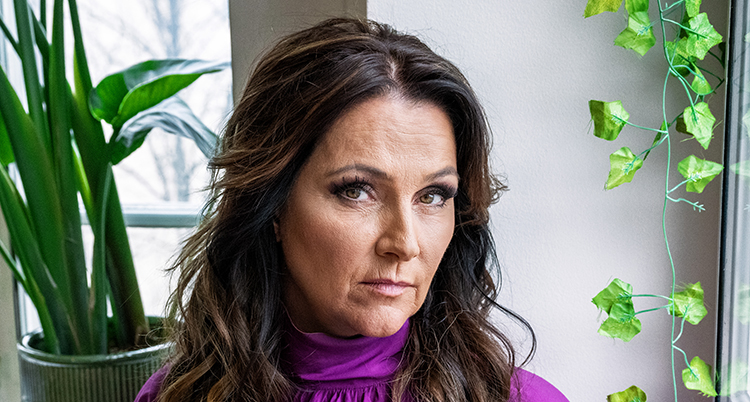 Hon tittar in i kameran, hon har en lila tröja. I bakgrunden syns gröna växter.