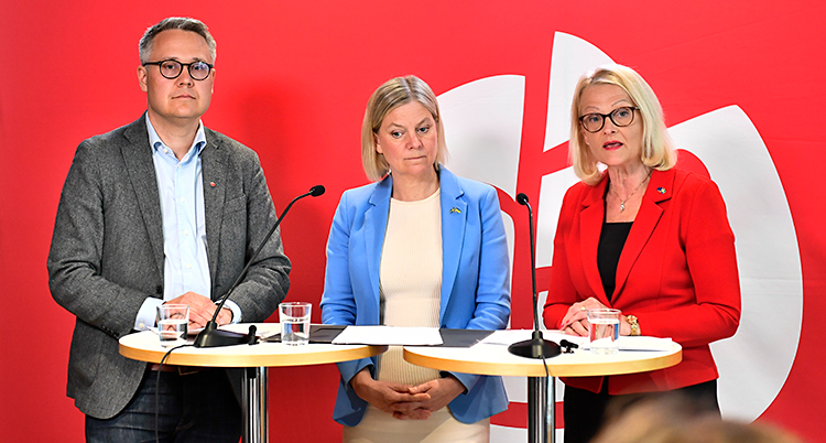 Tre personer står och pratar i mikrofoner på en träff med journalister.