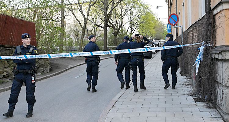 Flera poliser står bakom avspärrning på en gata.
