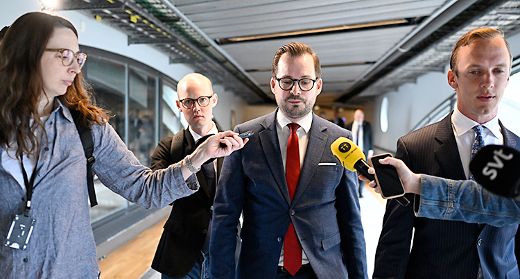 Han går i en korridor. Journalister går bredvid honom med mikrofoner.