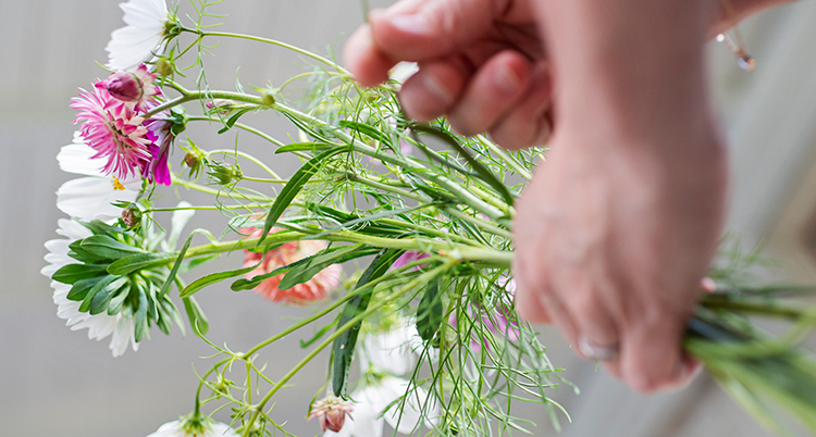 en hand håller en tunn bukett med blommor.
