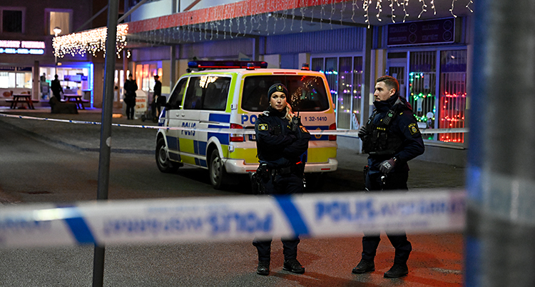 Det är mörkt. Två poliser står bakom avspärrningar.