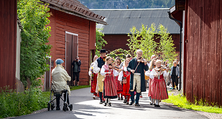 Några personer går genom byn. De spelar fiol och har folkdräkt.