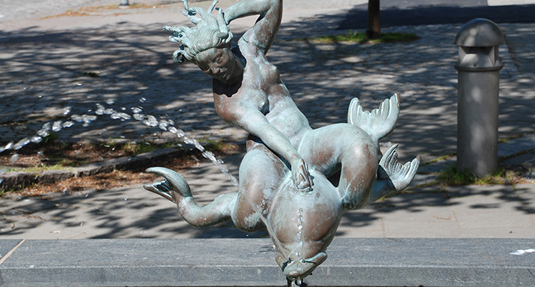En staty av en liten figur som rider på en fisk. Fisken sprutar vatten.