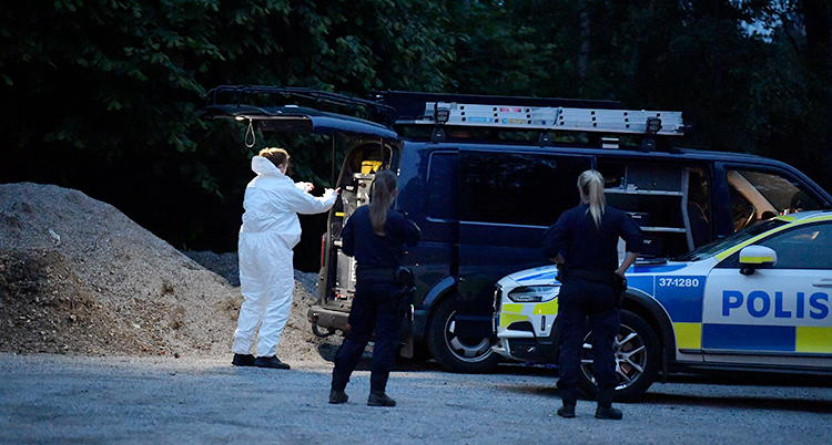 Polisens tekniker har vit skyddsdräkt. En polisbil och en svart liten minibuss syns också.