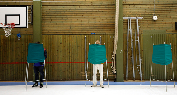 Tre personer står bakom gröna skärmar och kryssar i sina röster på ett kort.