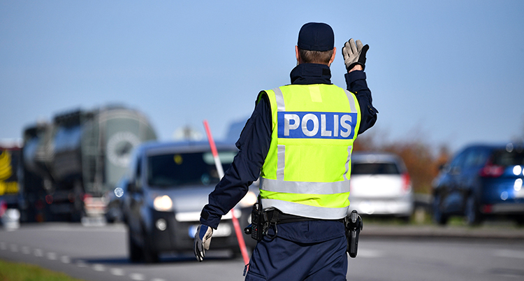 En polis stoppar en bil längs en väg.