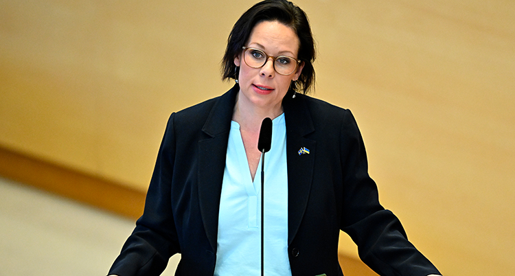 Hon står vid ett bord med mikrofoner och pratar.